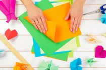 Hands folding colourful pieces of paper making origami rhinos that stand up.