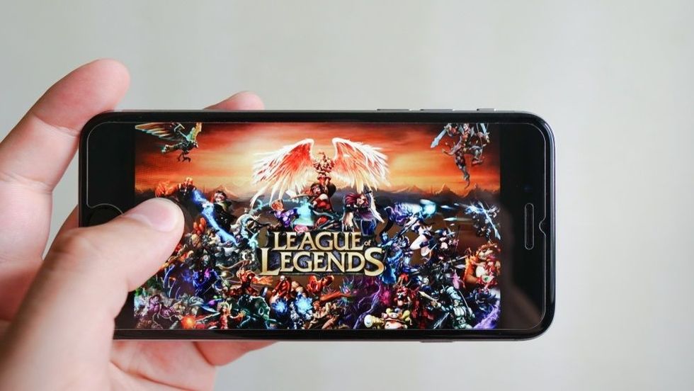 Hands holding a smartphone with League of Legends game on display screen.