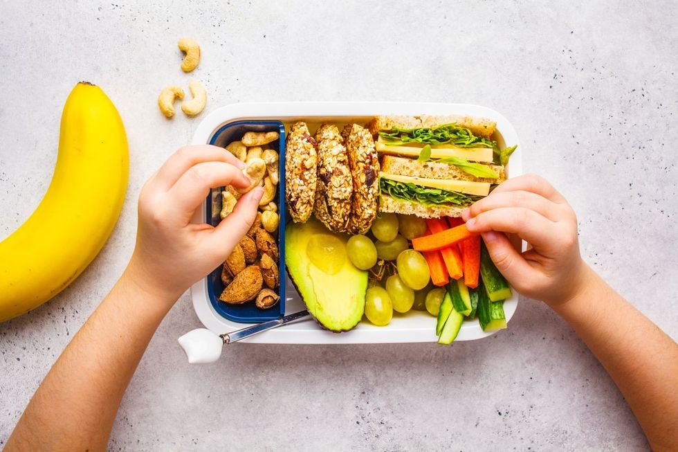 Hands preparing a balanced meal with a variety of healthy foods in a lunchbox next to a banana, inspiring to eat lunch that\u2019s both nutritious and delicious.