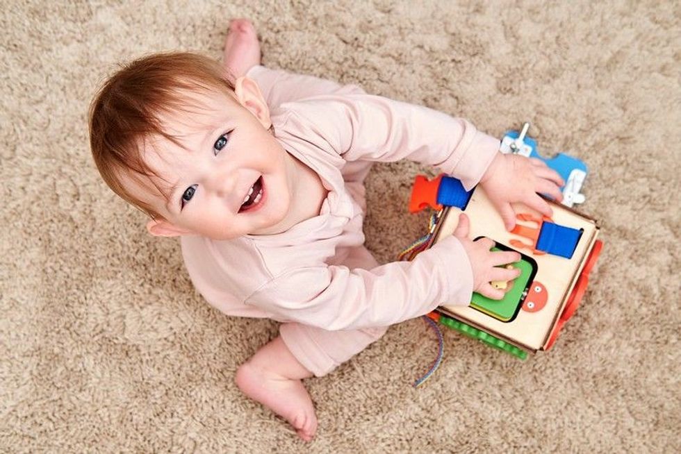 Happy baby boy James is playing with a busyboard cube on the nursery floor - Nicknames