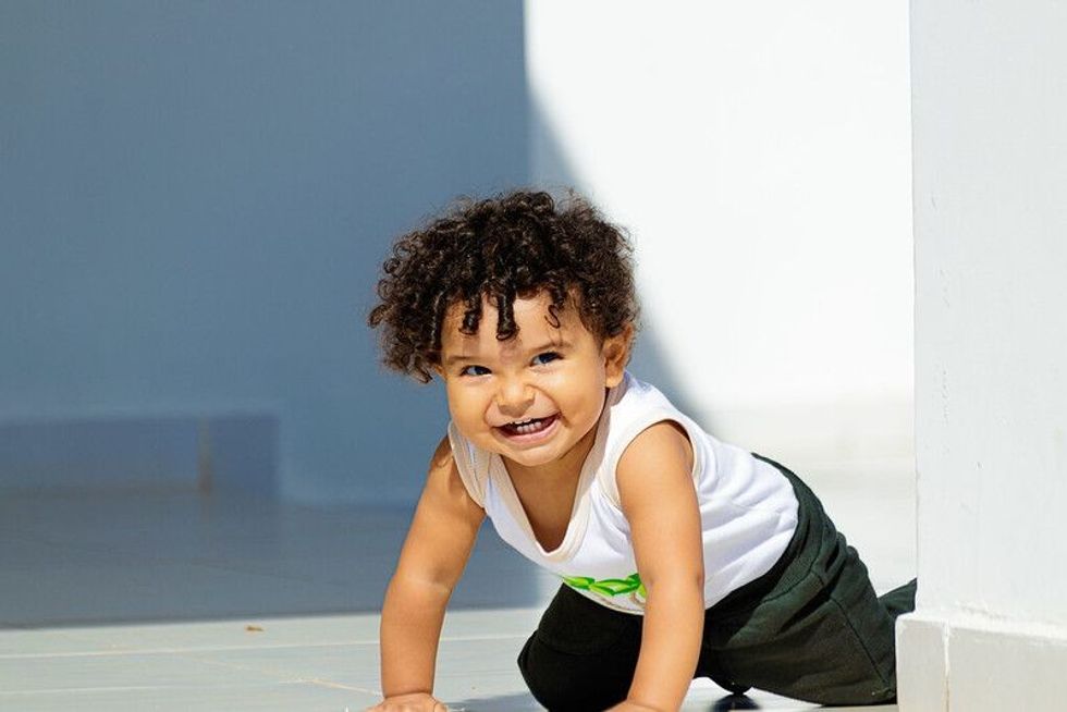 Happy baby boy with curly hair crawling outdoor