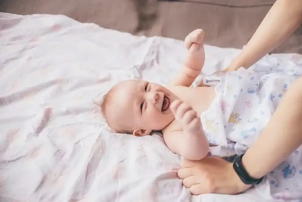 Happy baby lying on the bed smiling and giggling looking up at mum.