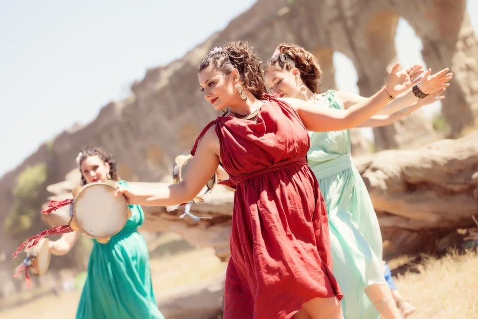 Happy beautiful girl dancing with another girls dressed in ancient roman greek historic style celebrating a pagan solstice and equinox rite and ritual with isntruments in an open field.
