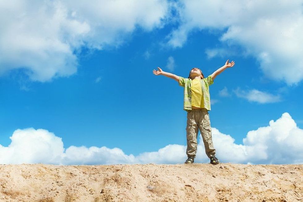 Happy child standing on the top with hands raised up