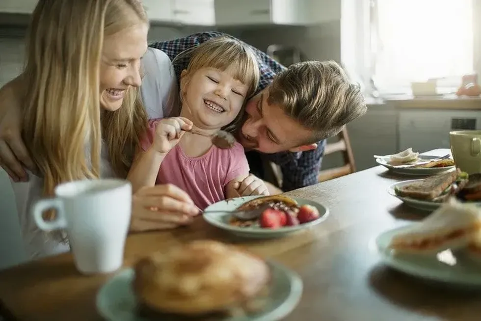 Happy family sat at the breakfast table laughing as they eat pancakes.
