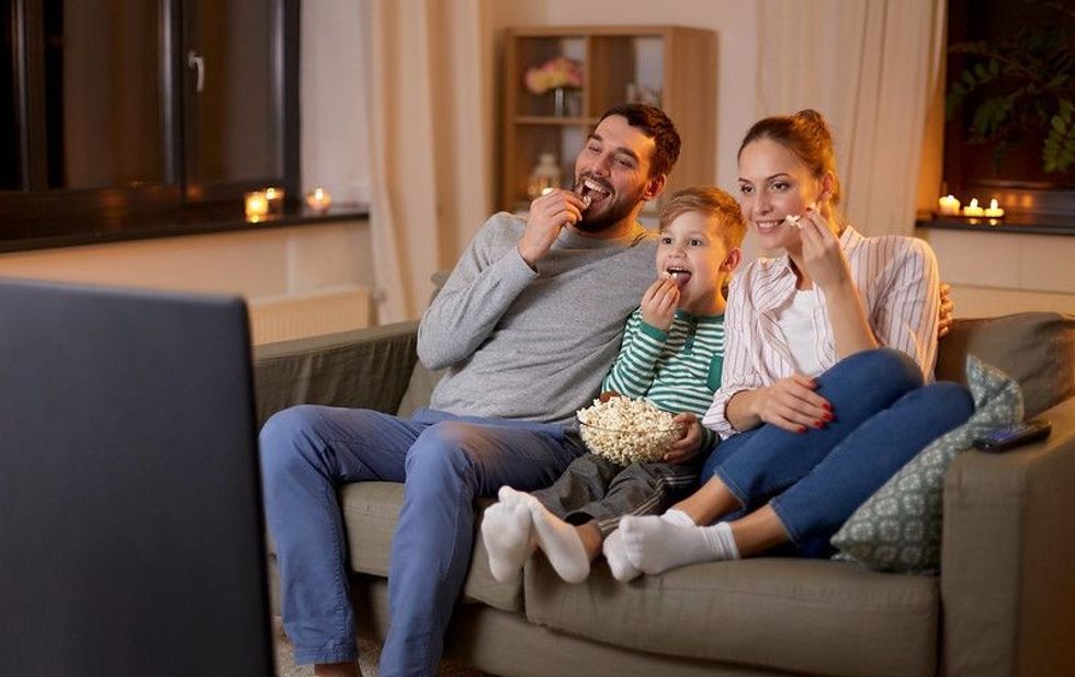Happy family watching tv and eating popcorn at home at night
