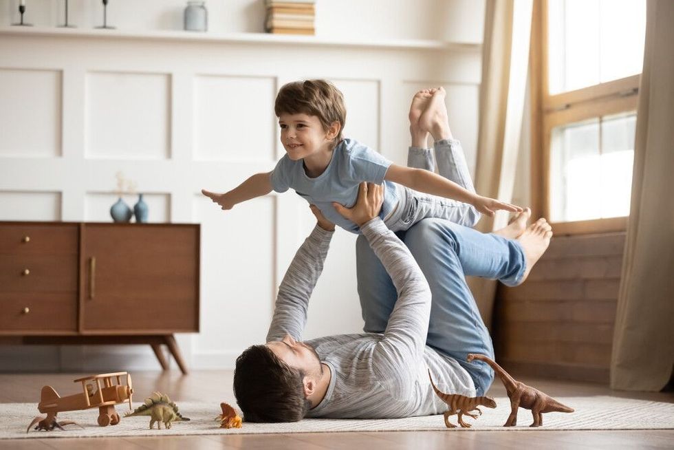 Happy father lying on carpet floor, lifting excited happy little child son at home