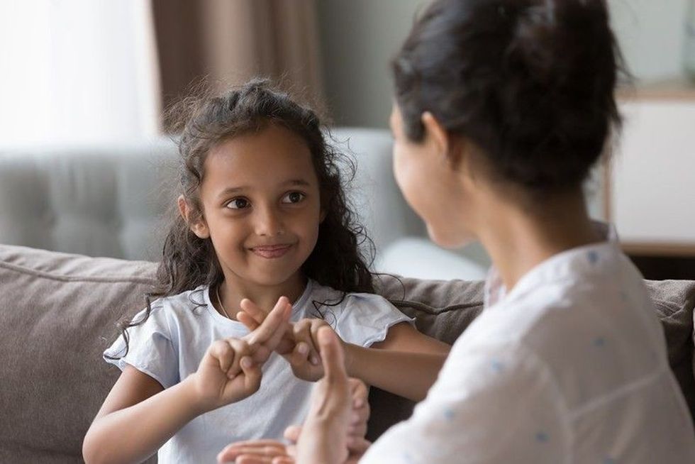 Happy Indian kid girl talking to mother, using hands, fingers, speaking sign languages representing ASL Day.