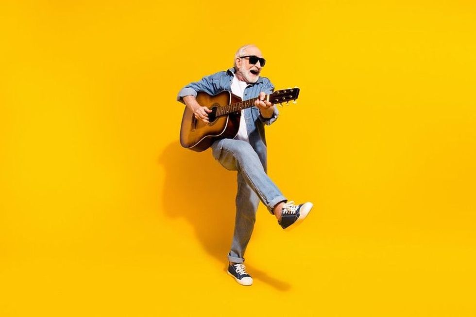 Happy old man feeling young and energetic holding a guitar