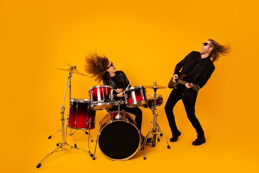 Heavy metal male guitarist and female drummer jamming to the tunes in yellow background studio