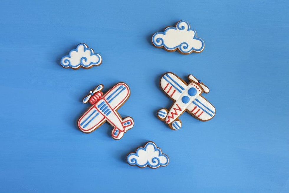 Homemade gingerbread cookies in the shape of airplanes and clouds on a blue table.