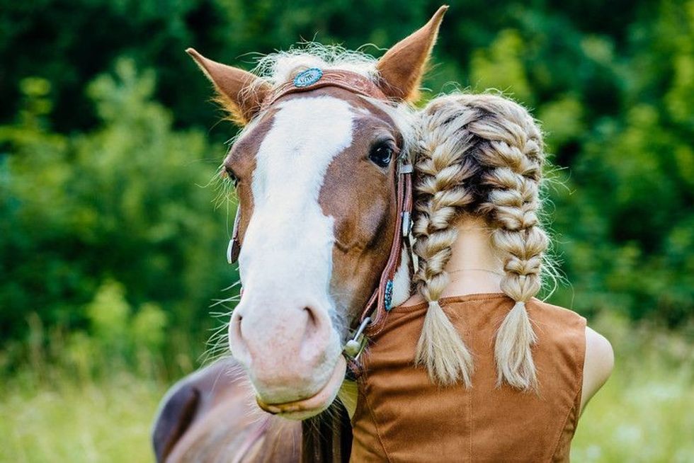 Horse and young  woman with two braids hugging. 