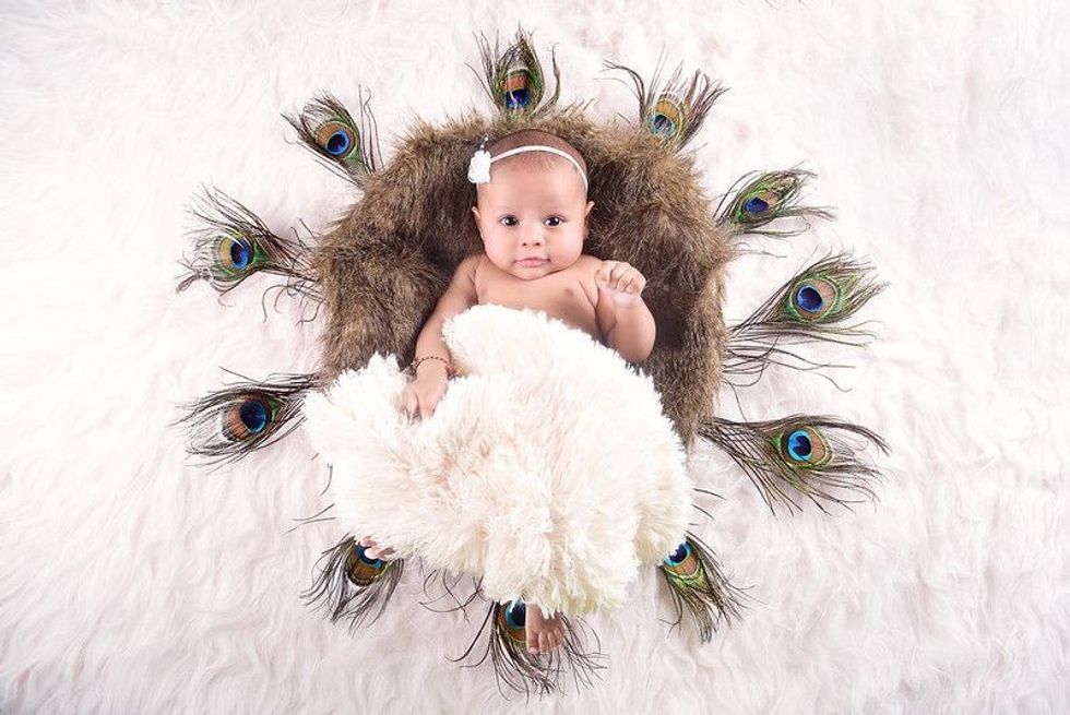 Indian newborn baby in a fur basket surrounded by peacock feathers