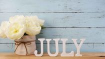 'July' letters with off-white flowers and a blue background
