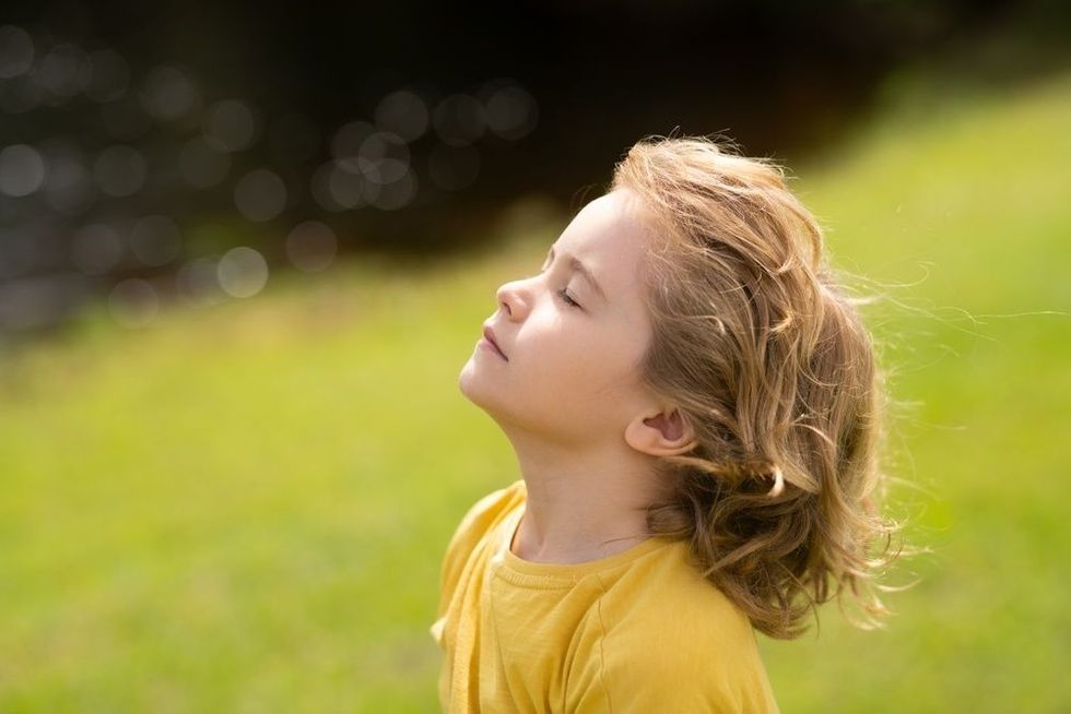 Kid put face to the sun, closed her eyes and feeds energy of nature.