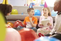 Kids at a birthday party sat on the floor playing pass the parcel.