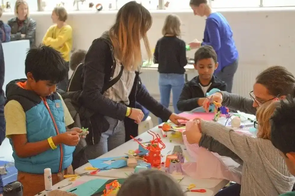 Kids in a classroom sat around the desk doing arts and crafts.
