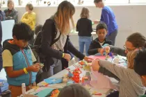 Kids in a classroom sat around the desk doing arts and crafts.