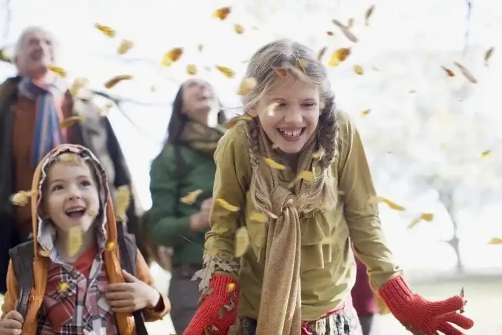 Kids smiling enjoying the orange leaves of autumn.