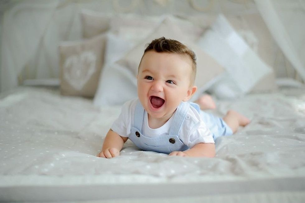 Laughing baby boy lying on bed.