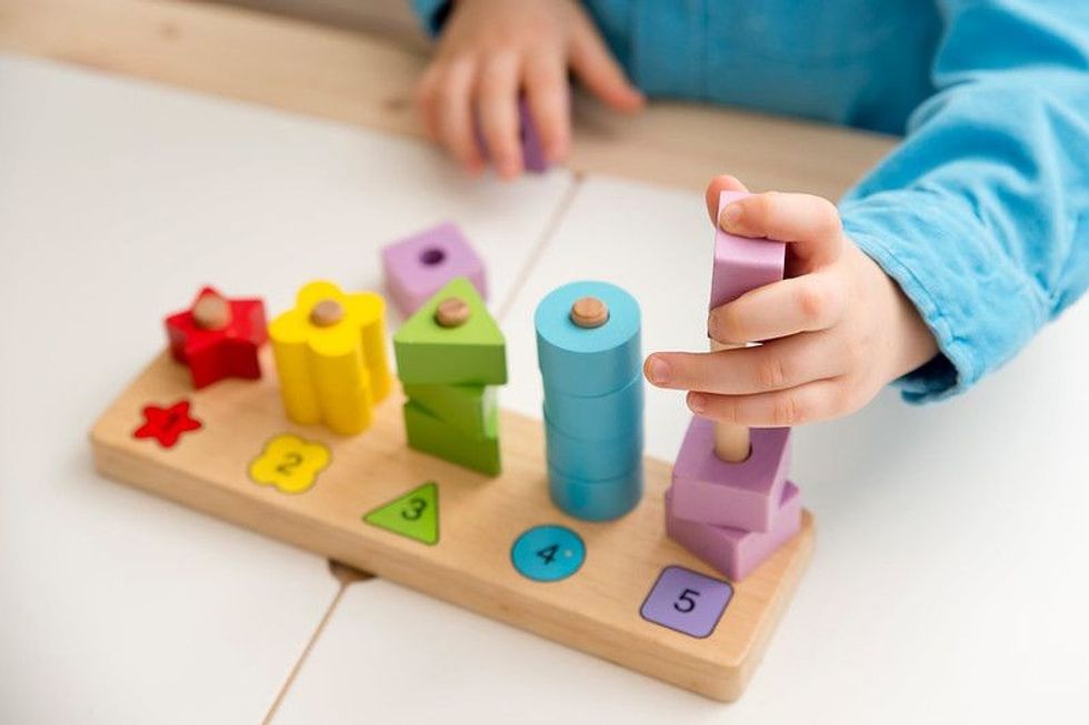 Learning counting, shapes and colors. Montessori type implement. wooden toys. Boy puts on figures on poles.