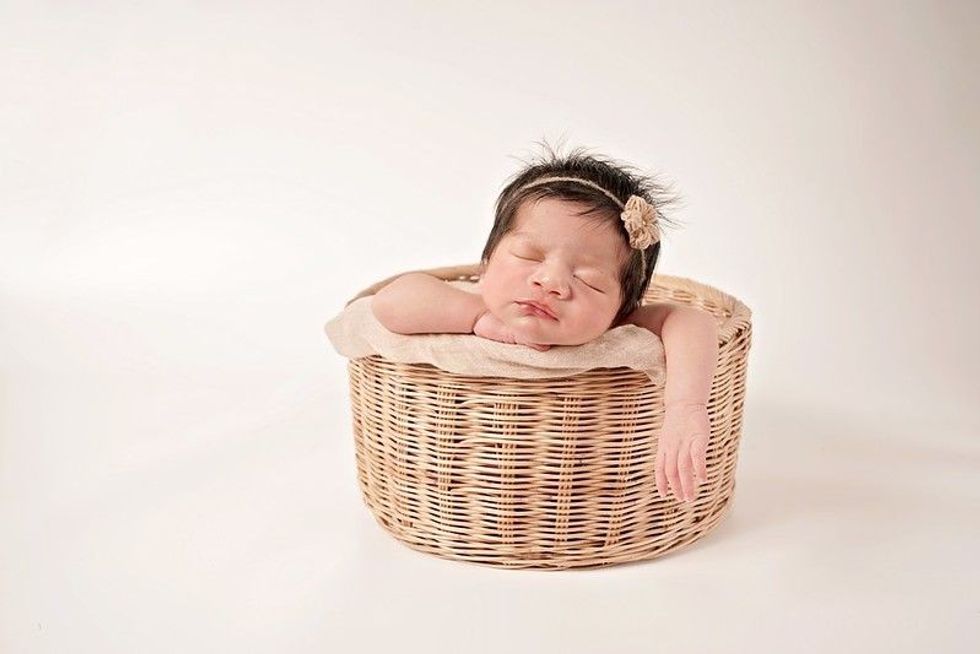 Little baby girl sleeps with her chin on hand in a rattan basket