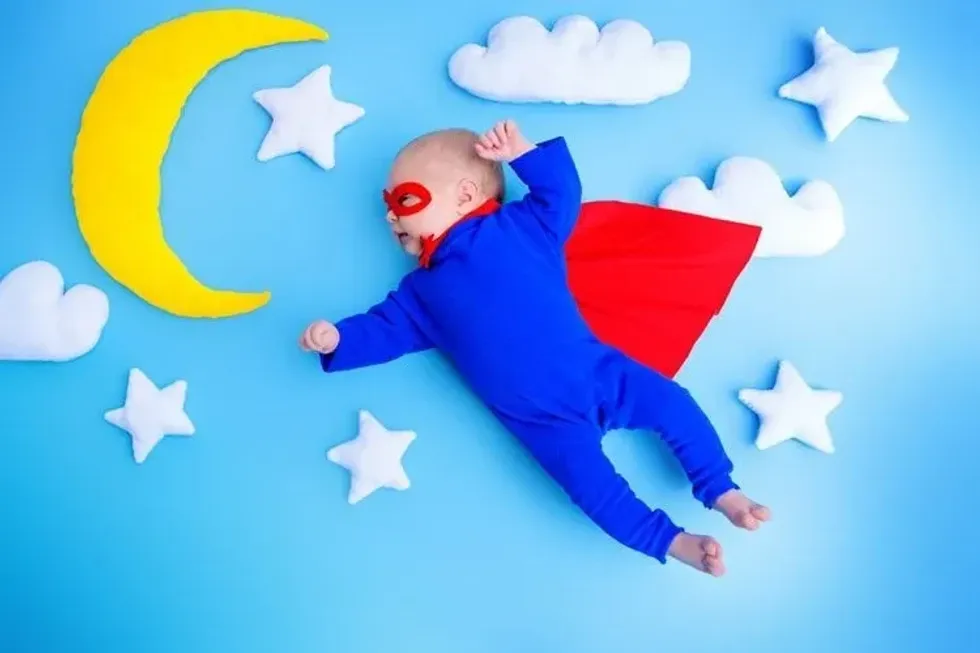 Little baby superhero with red cape flies through the night sky