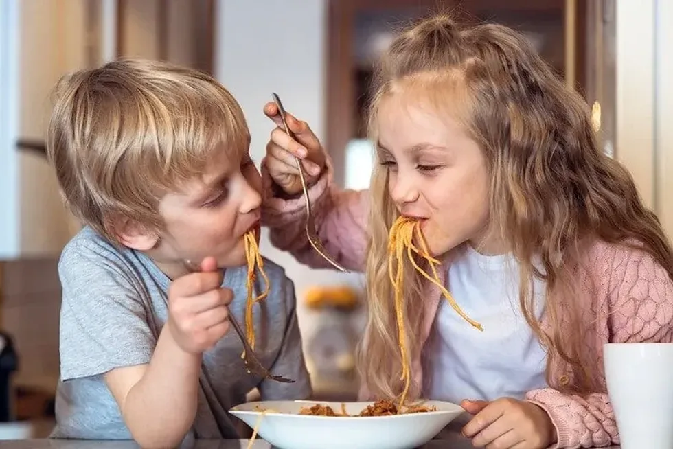 Little boy and girl amused while eating spaghetti.