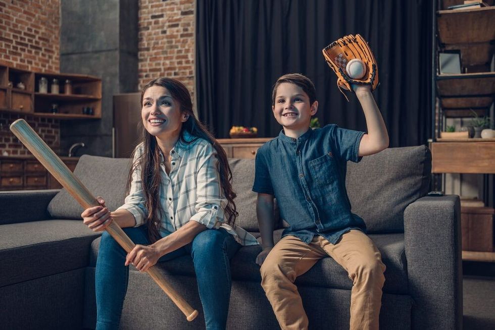 Little boy and his mother sitting on couch in living room with baseball bat and mitts