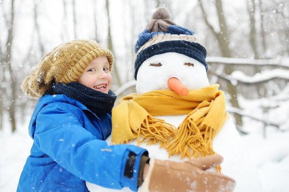 Little boy building snowman in snowy park.