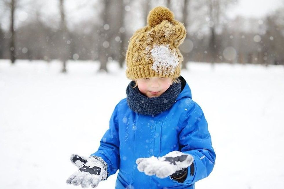 Little boy having fun playing with fresh snow during snowfall.