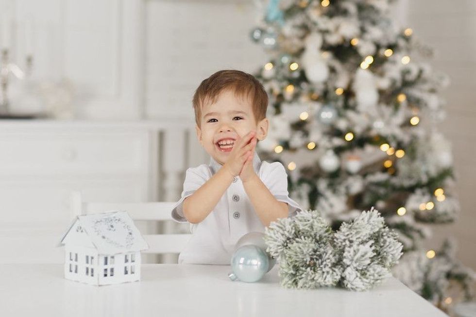 Little boy sitting next to Christmas tree on dining table