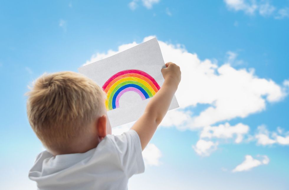 Little child holding up a rainbow painting in the sky.