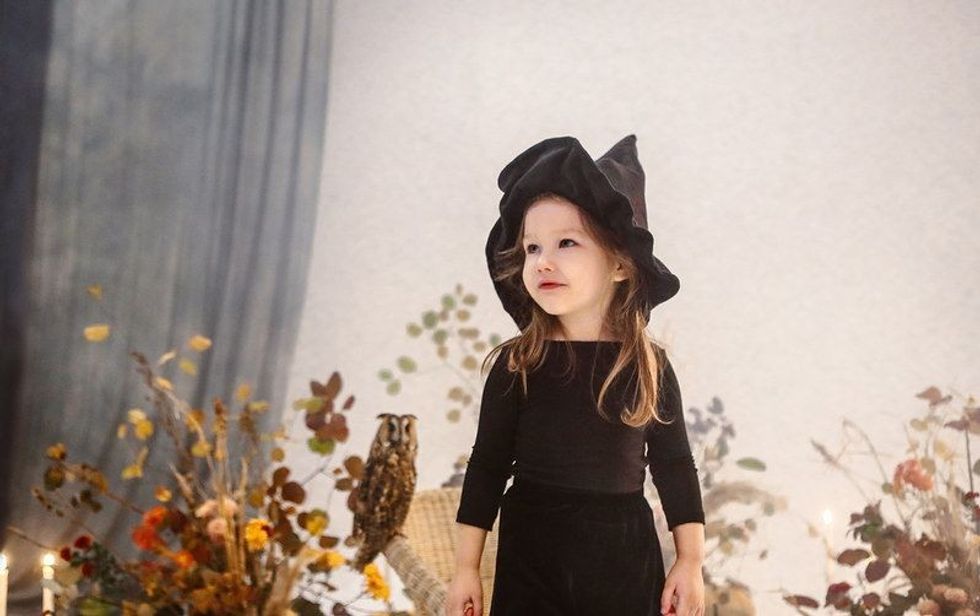 Little cute girl with long hair standing on scene in black dress and hat with autumn decorations