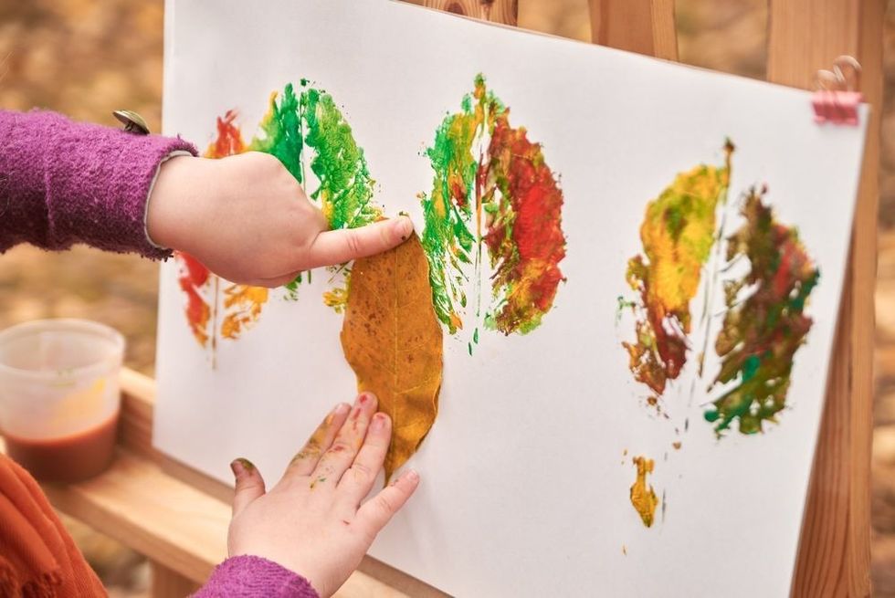 Little girl artist paints autumn leaves in the park