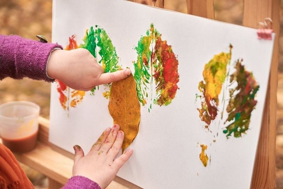 Little girl artist paints autumn leaves in the park