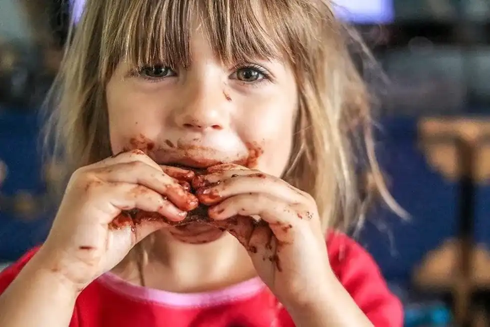 Little girl eating chocolate has got chocolate all around her mouth and on her hands.