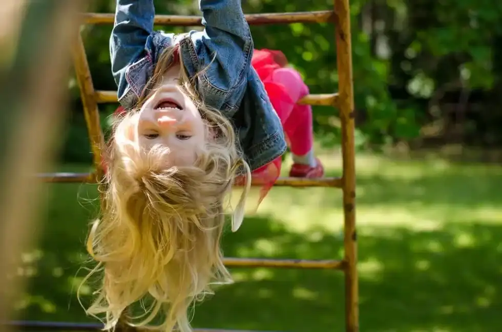 Little girl hanging from a climbing frame in the park on a day out in Derby.