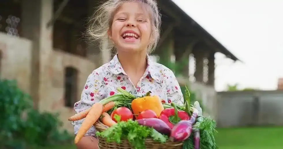 Little girl holding a basket of vegetables smiling.