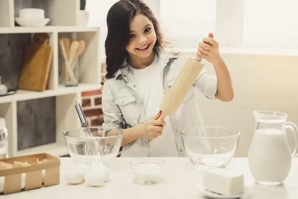 Little girl holding a rolling pin and smiling in the kitchen as she makes a Postman Pat cake.