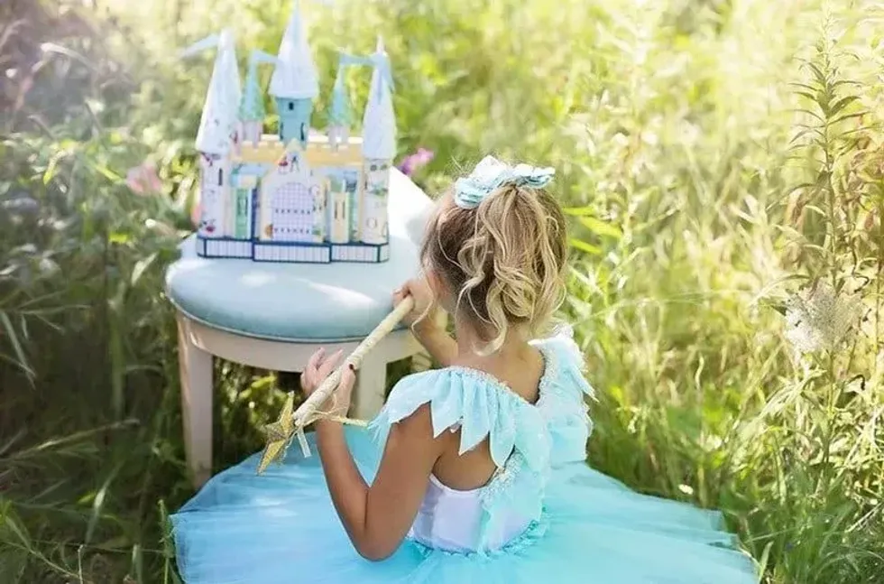 Little girl in blue fairy gown sitting in the grass with her mini blue castle.