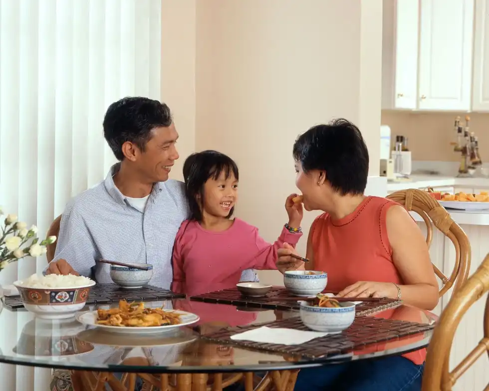 Little girl is feeding her mother while having food with her parents