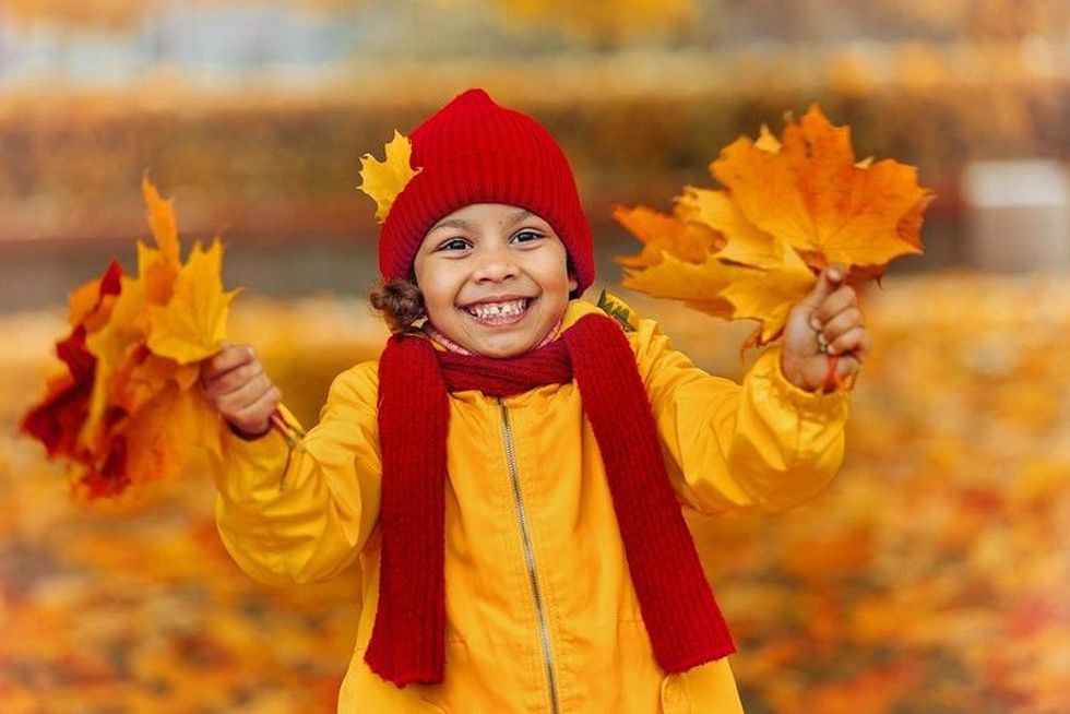 Little girl wearing yellow jacket holding maple leaves