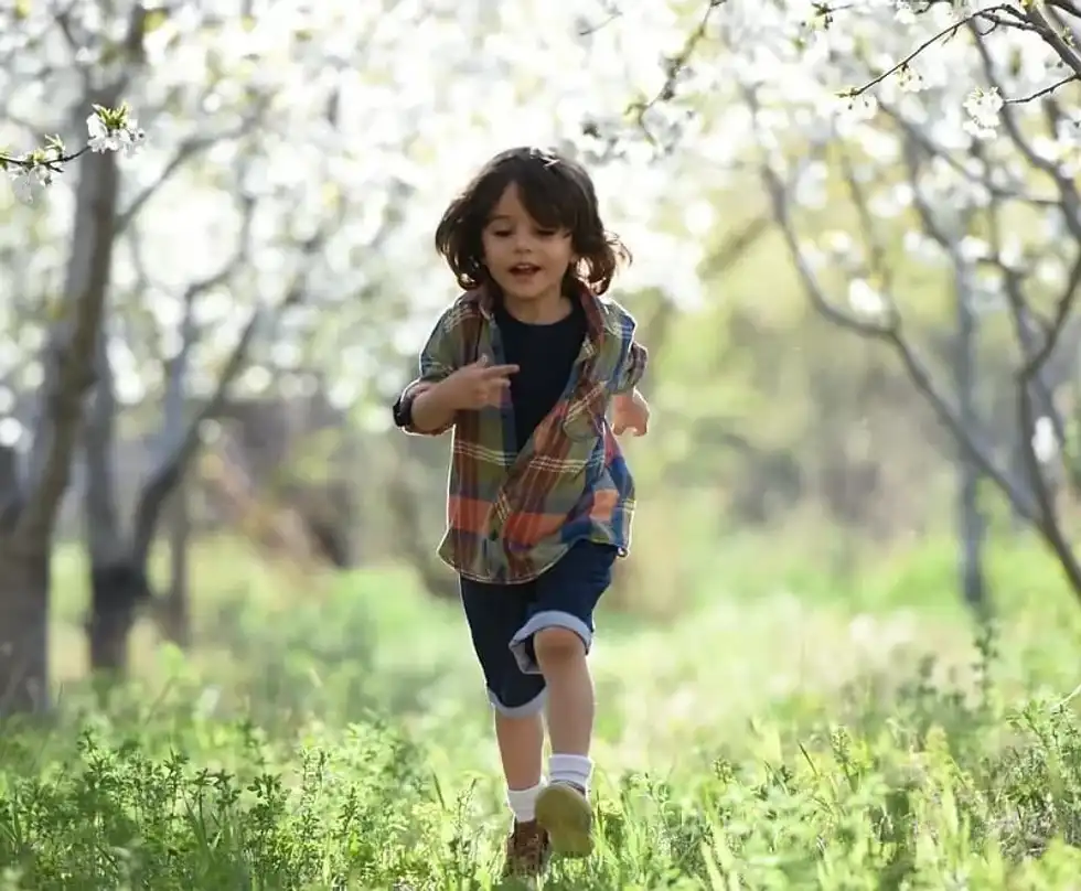 Little kid running through the trees in the woods.