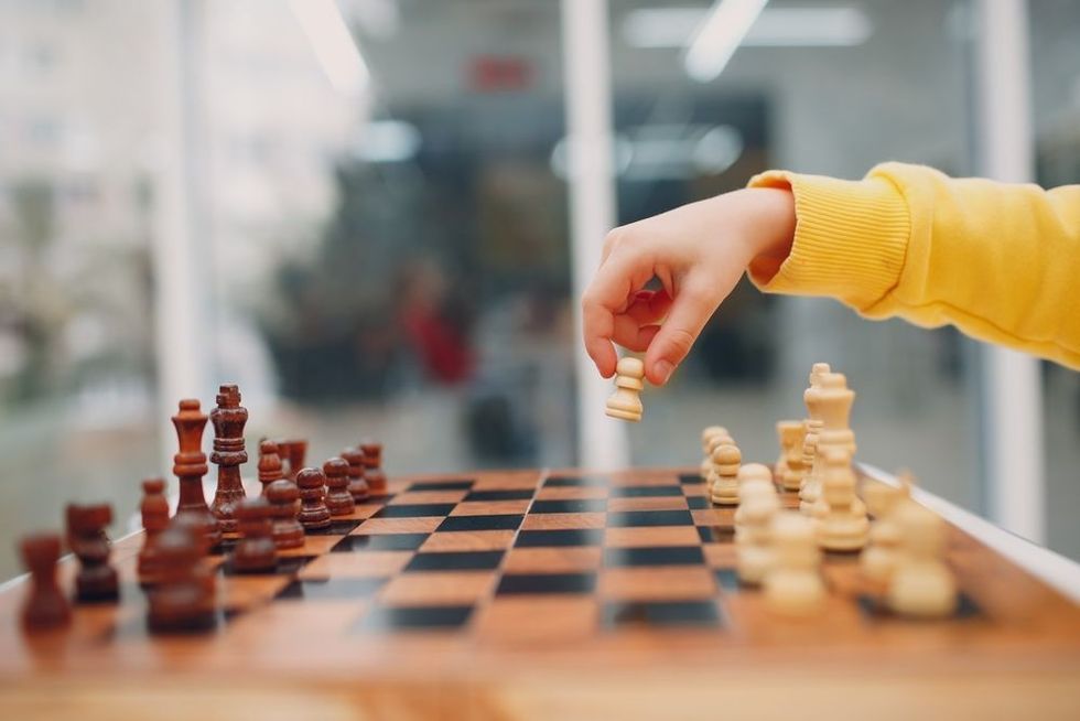 Little kids playing chess at kindergarten or elementary school. Hand holds chess figure close up.
