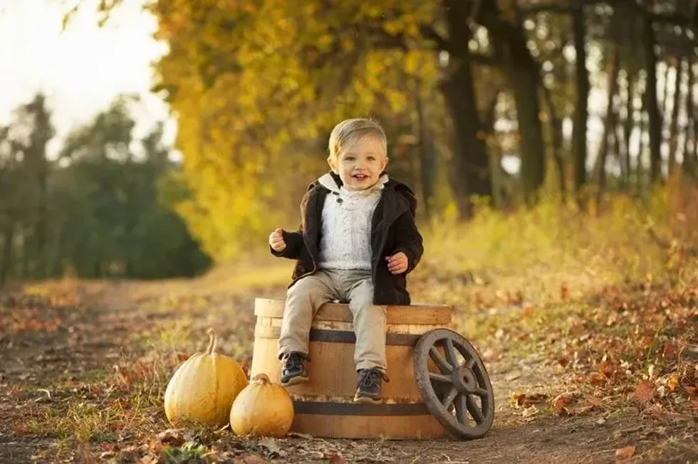 Little smiling boy sits on a wooden barrel in the autumn forest