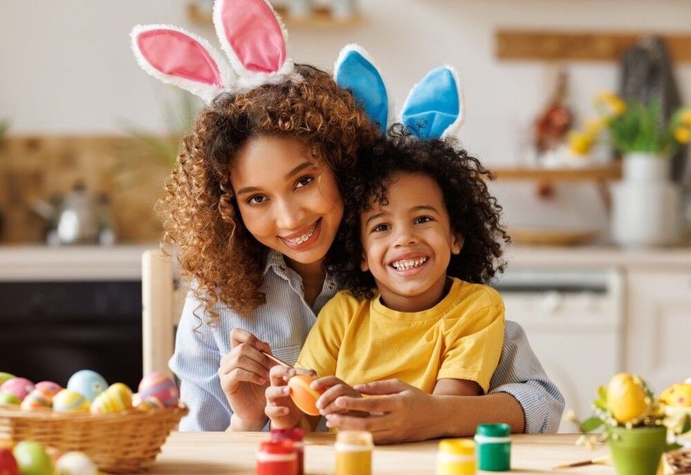 Loving young mother teaching happy little kid to dye and decorate eggs with paints for Easter holidays 