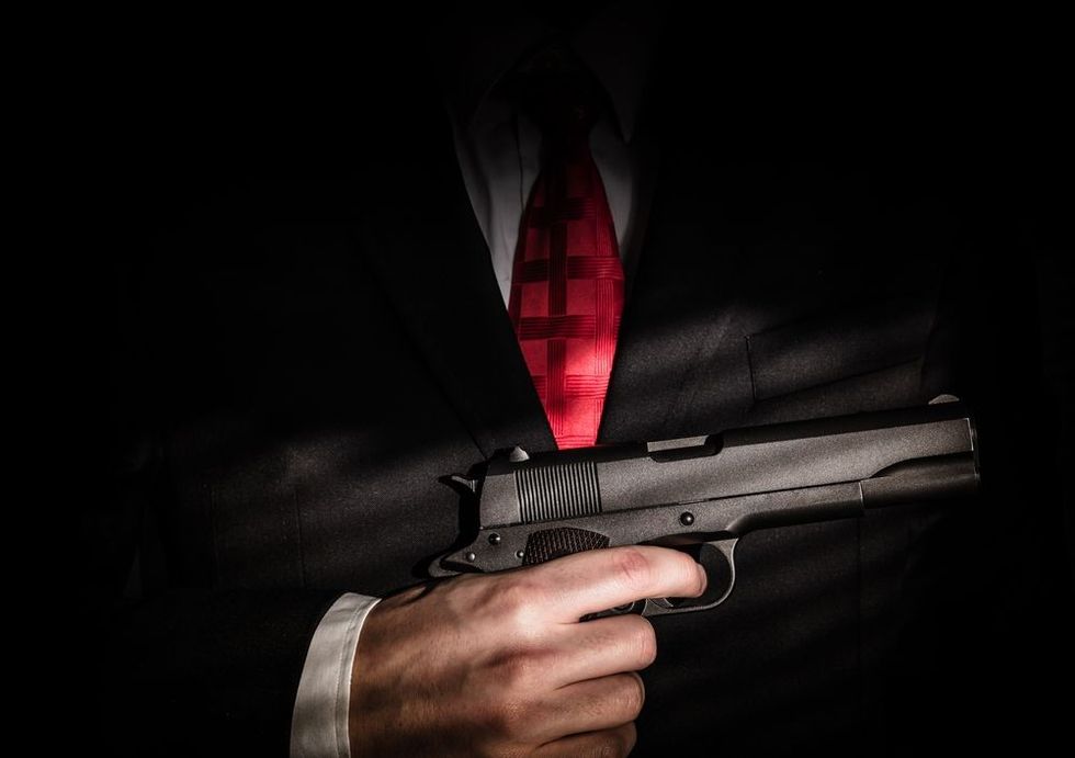 Mafioso holds pulled out gun, isolated on dark background