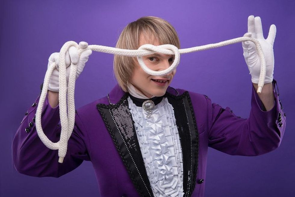 Magician wearing splendid violet costume and white shirt making a knot using the white rope.