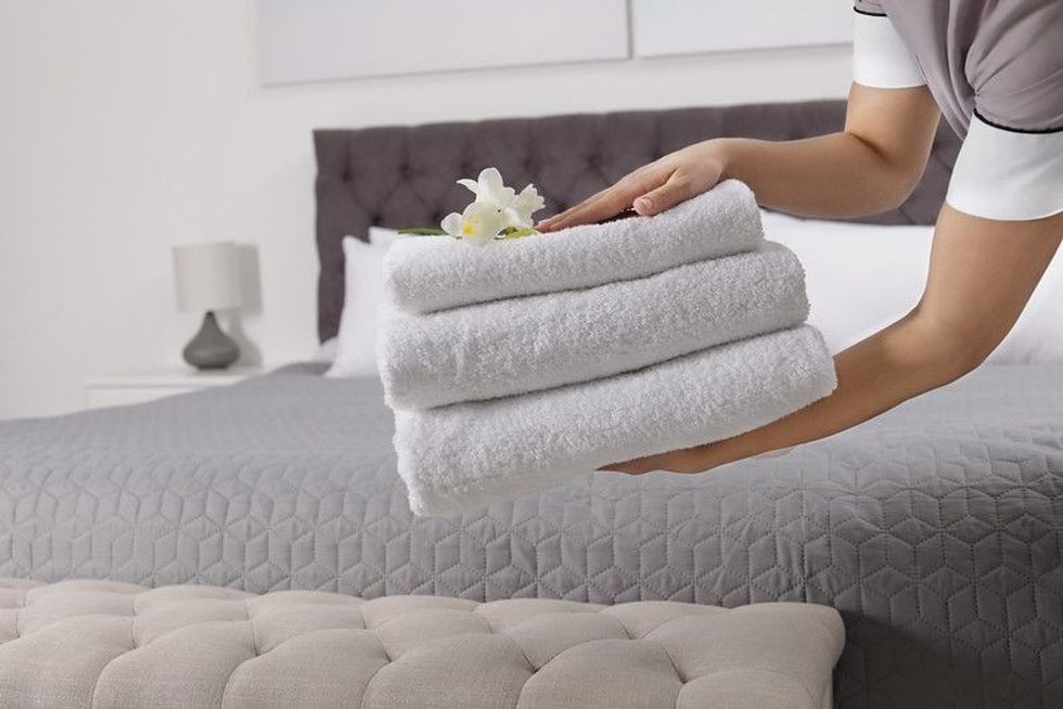 Maid holding fresh towels with flowers in hotel room.